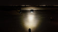Load image into Gallery viewer, A portable scene light emitting a powerful beam of light across a dark landscape, with a person visible in the foreground.