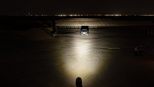 A portable scene light emitting a powerful beam of light across a dark landscape, with a person visible in the foreground.